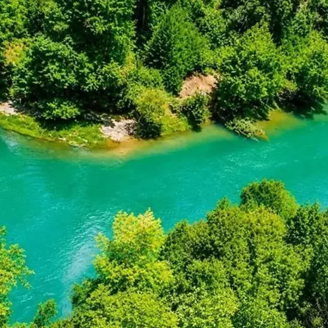 A turquoise river winding through dense green forest, seen from above.